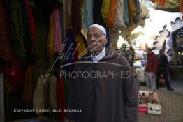 Image du Maroc Professionnelle de  Mohammed Ennaji âgé de soixante-dix ans, pose devant son atelier à Marrakech, il a commencé à pratiquer ce métier de teinturier à l’âge de dix ans, cela lui fait soixante ans de métier un des plus ancien voir le vétéran des teinturiers, son atelier est situé au centre du Souk des Teinturiers, appelé souk Sebbaghine, l'un des plus pittoresque de Marrakech situé dans la Médina, non loin de la source Mouassine, où quelques petits ateliers pratiquent encore de nos jours la teinture traditionnelle. Ce lieu très prisé des touristes et amateurs photos qui désire ardemment des images extrêmement colorées. Avec le temps il est devenu presque une des attractions touristique qui vaut le détour. Derrière Si Mohammed Ennaji des écheveaux de laines sèchent au soleil suspendu en l’air ou le long des murs, le 8 Décembre 2018. (Photo / Abdeljalil Bounhar) 